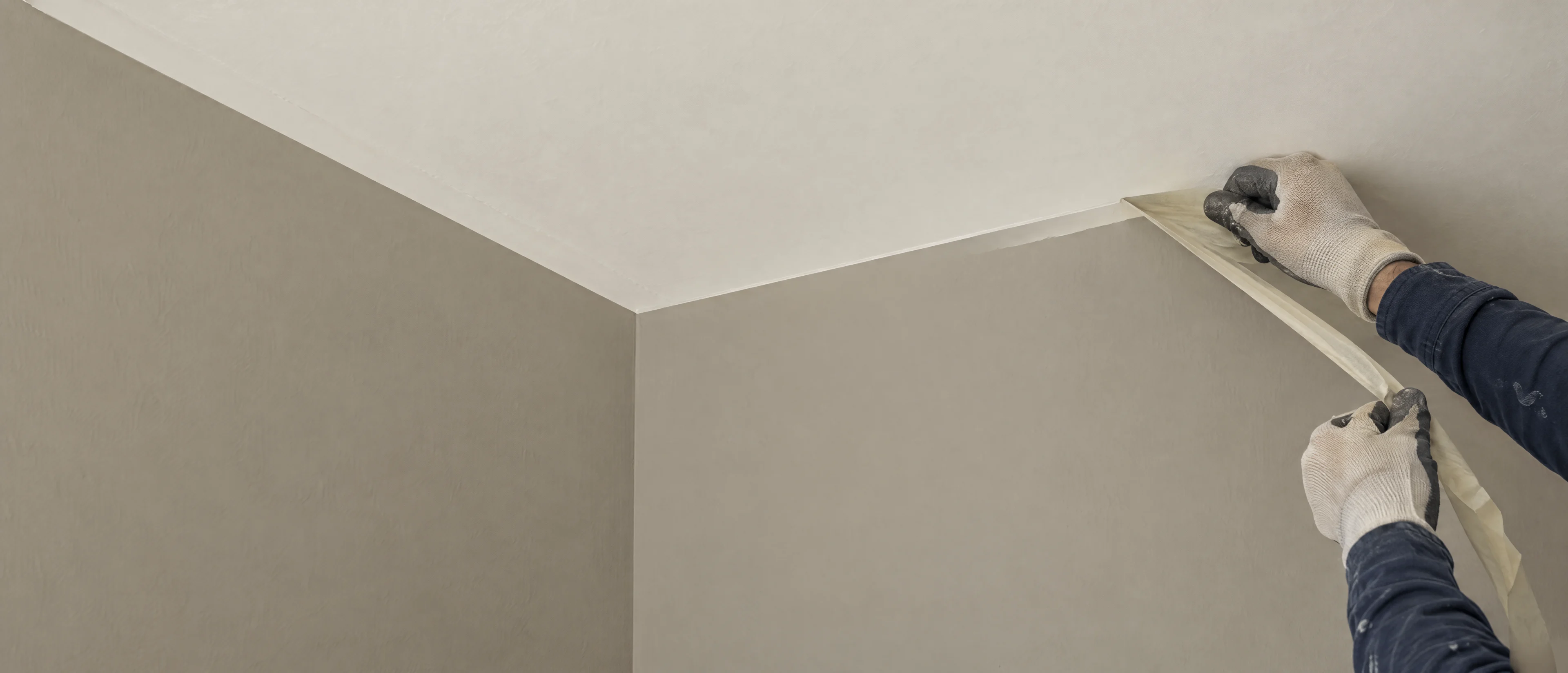 Klebeband wird an der Kante zwischen grauer Wand und weißer Decke abgezogen